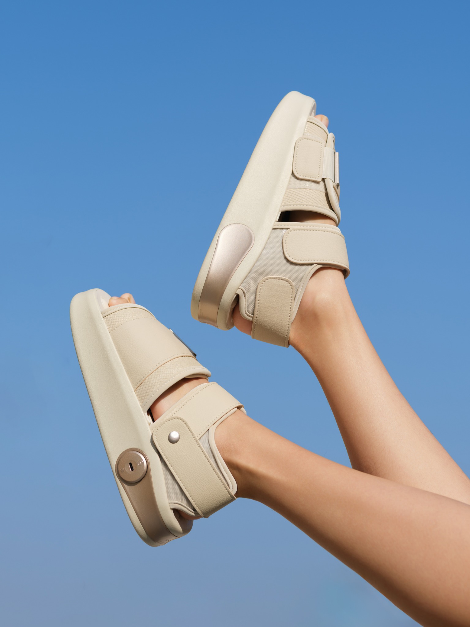 Feet wearing cream F1 massagers against a clear blue sky